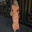 Woman in a floral dress standing on a street with a decorative door in the background