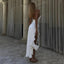 Woman in a white dress standing in a classical architecture setting with curtains.
