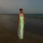 Woman in a glowing dress standing on a beach at dusk