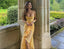 Woman in a yellow dress standing in a garden with stone arches and greenery.