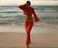 Woman in a red patterned outfit standing on a beach with ocean waves in the background