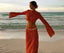 Woman in a patterned outfit standing on a beach with ocean waves in the background