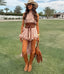 Woman in a pink dress and cowboy hat standing on grass with palm trees in the background