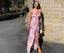 Woman in a floral dress standing against a brick wall.